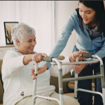 Caregiver supporting a senior woman walking safely in a bright, modern residential care setting