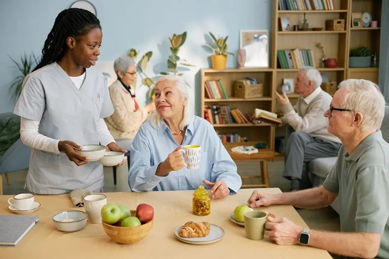 Caregiver serving tea and fruit to older adults at a table